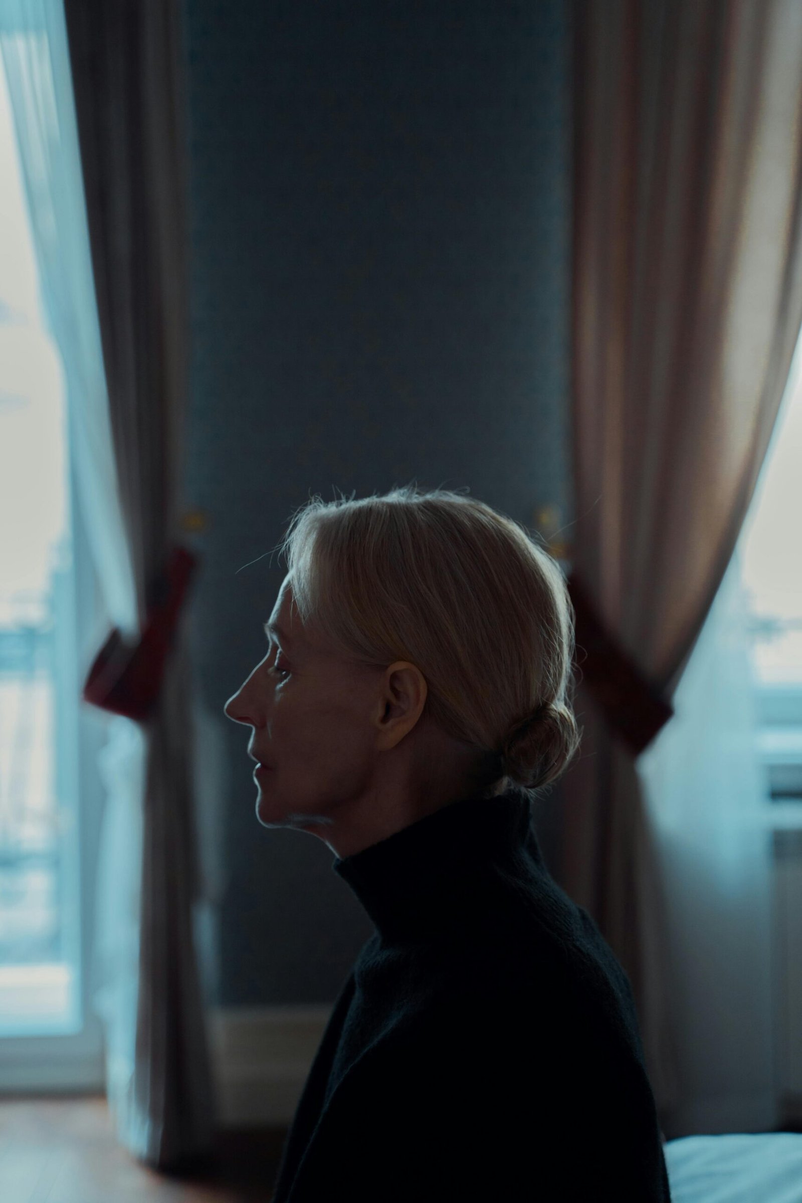 Profile of a confident woman over 50 sitting peacefully in a softly lit room, embracing solitude and self-reflection.
