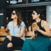 woman in black and blue sleeveless dress holding glass of beer sitting on bench