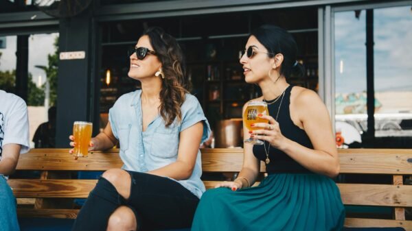 woman in black and blue sleeveless dress holding glass of beer sitting on bench