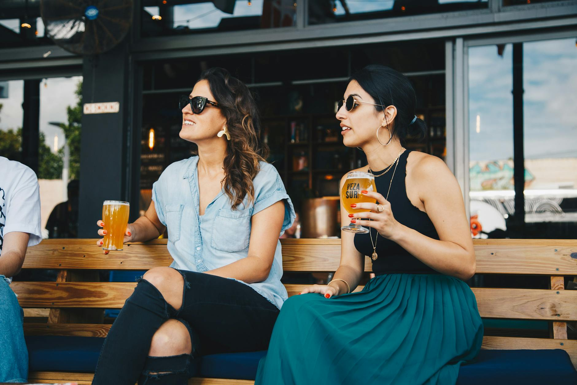 woman in black and blue sleeveless dress holding glass of beer sitting on bench