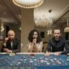 a woman and men sitting at a gaming table with stacks of casino tokens