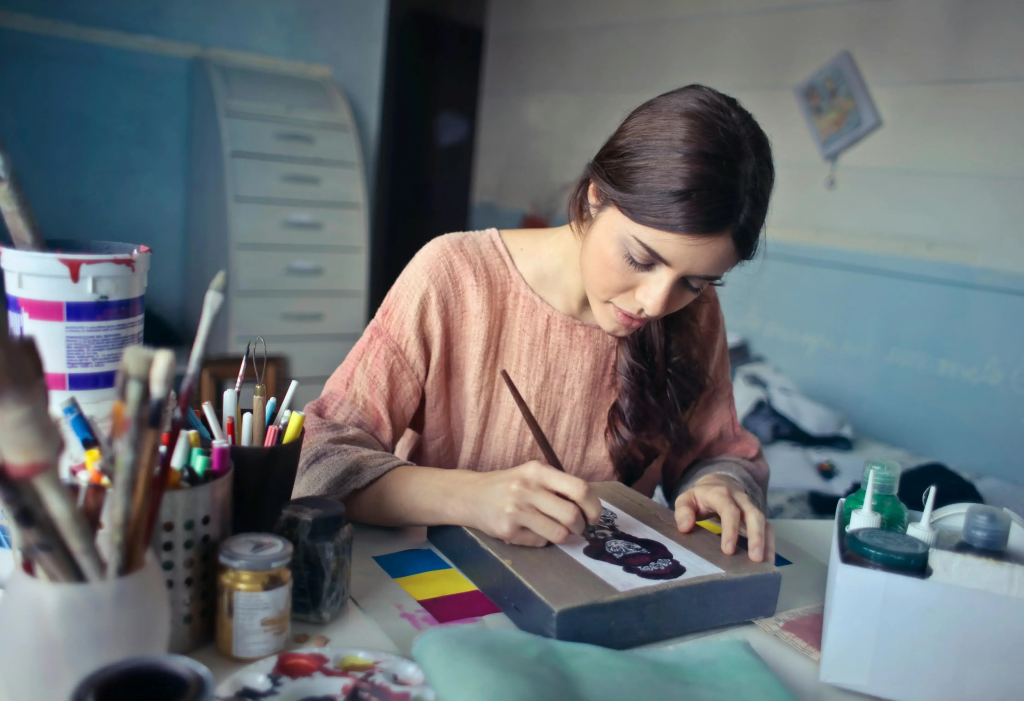 Artist painting at her desk while building a creative offer for the $100 start.