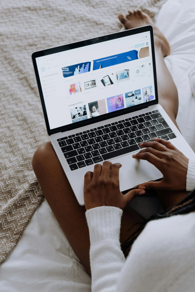 Person working on a laptop in bed, designing graphics in Canva as part of the modern creative starter stack.