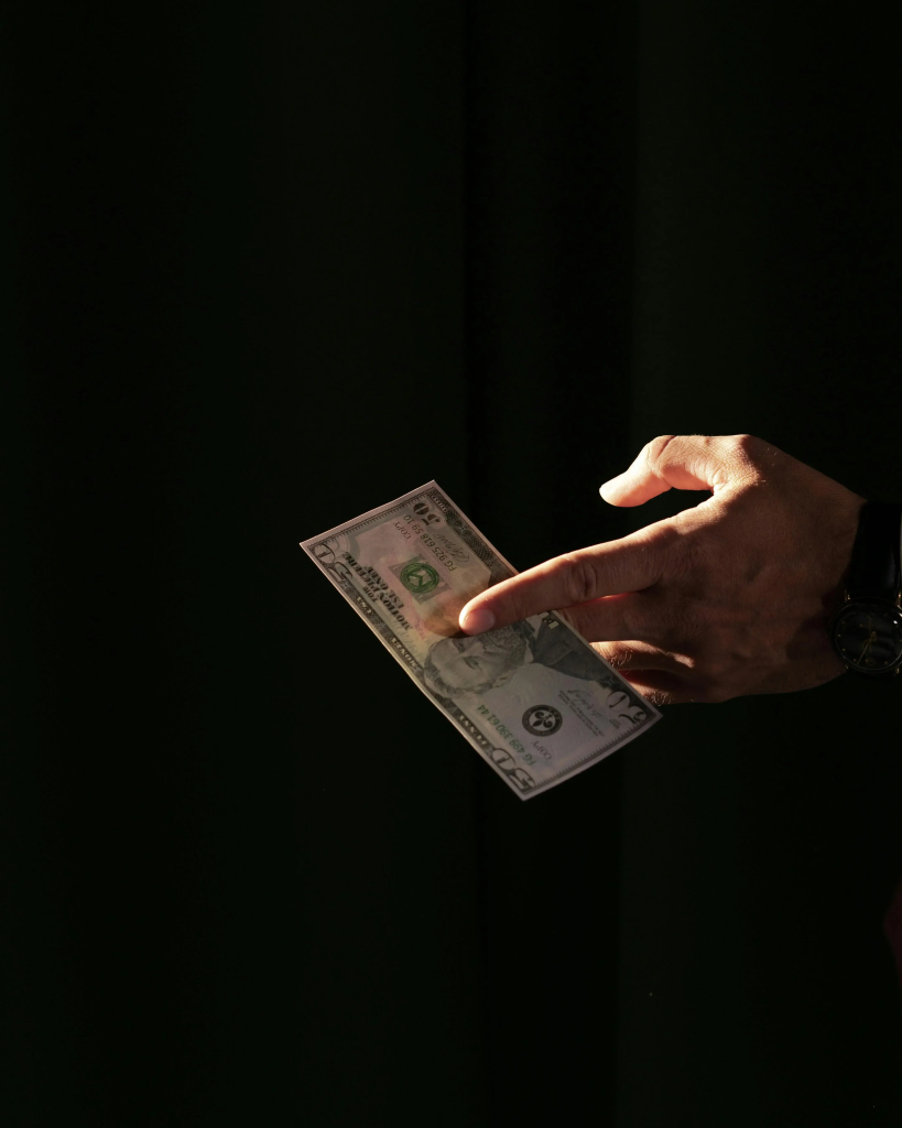 Hand holding a five-dollar bill in low light, symbolizing savings regret and missed money decisions