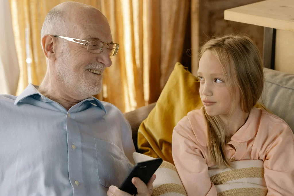 Older dad in his 50s smiling while spending quality time with his daughter on the couch.