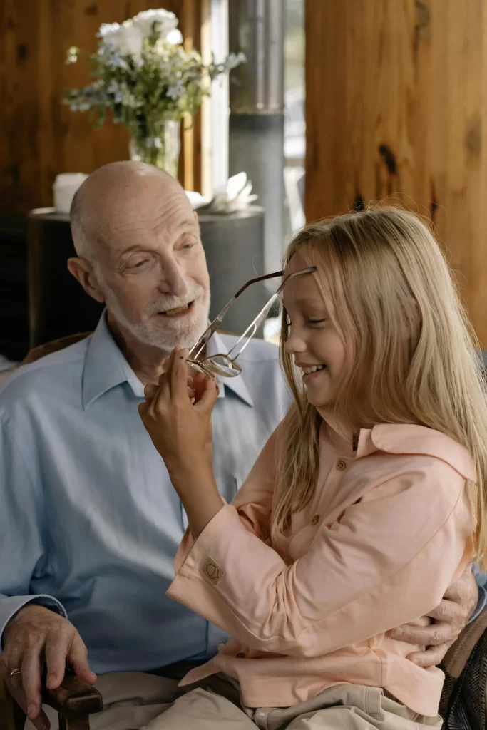 Dad in his 50s laughing with his daughter as she tries on his eyeglasses.