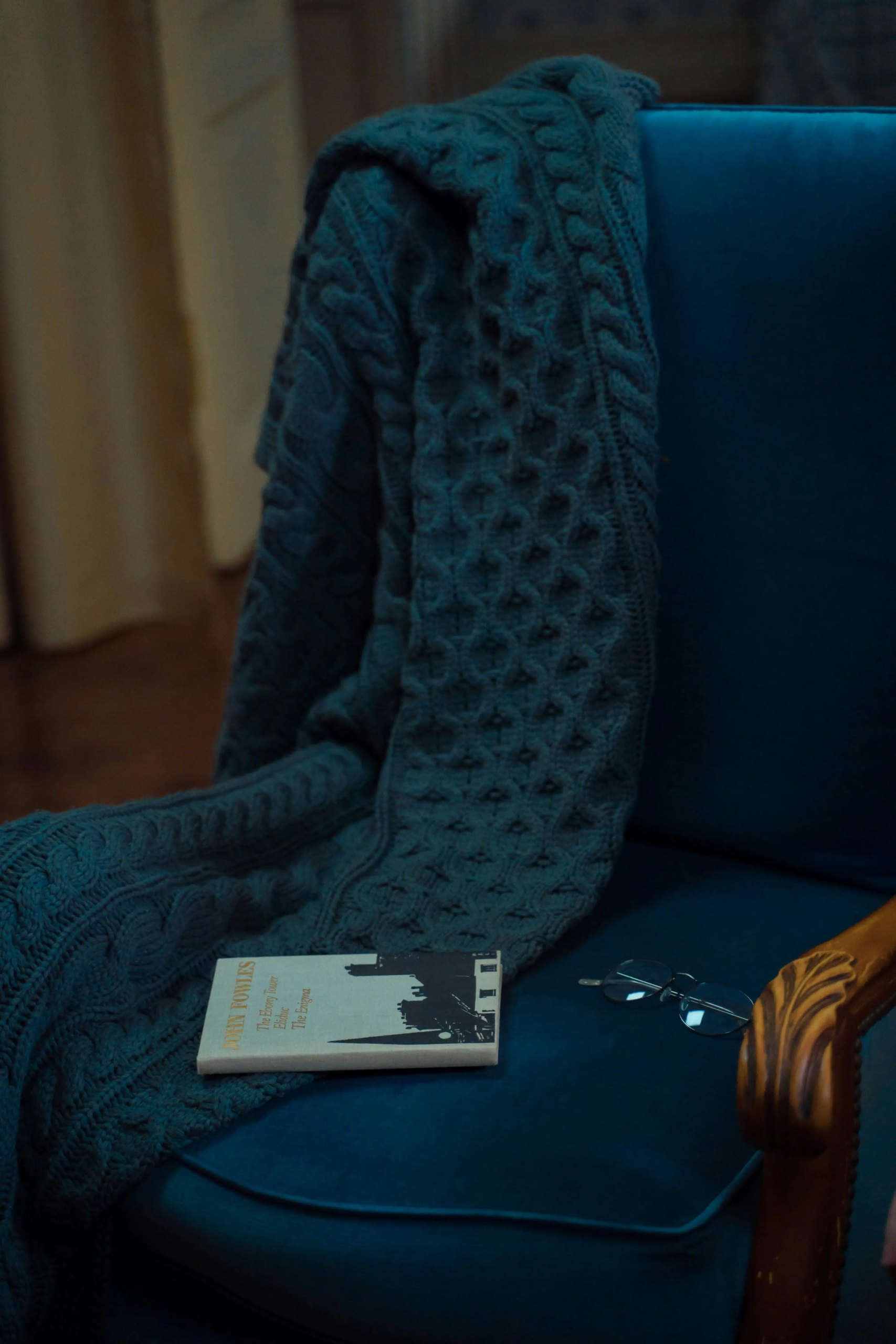 A cozy blue armchair with a knitted blanket, an old book, and reading glasses resting on the seat, creating a nostalgic living-room atmosphere.