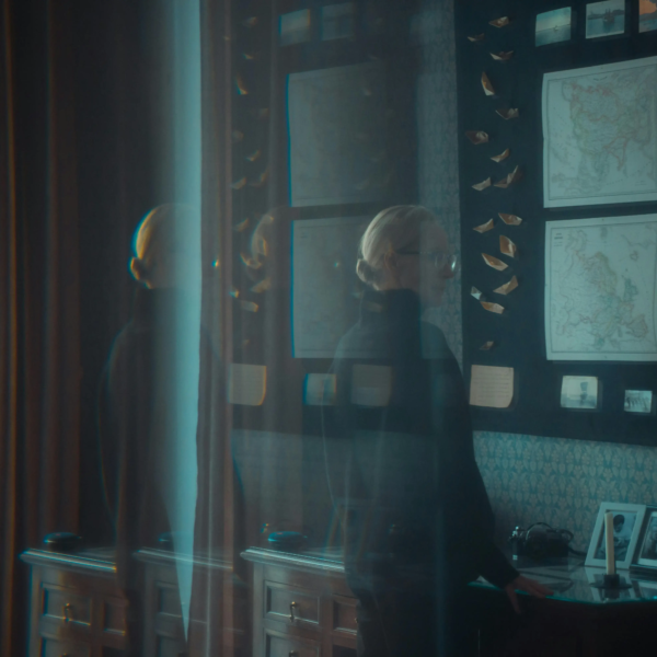 A vintage study room with maps, photos, and collectible items on the wall, captured with a blurred silhouette of a person passing by.