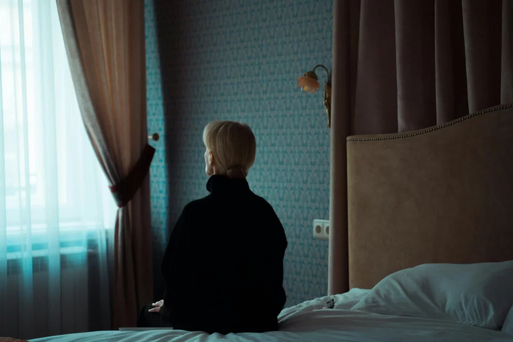 Woman sitting on a bed facing the window, quietly reflecting during her midlife brain reset.