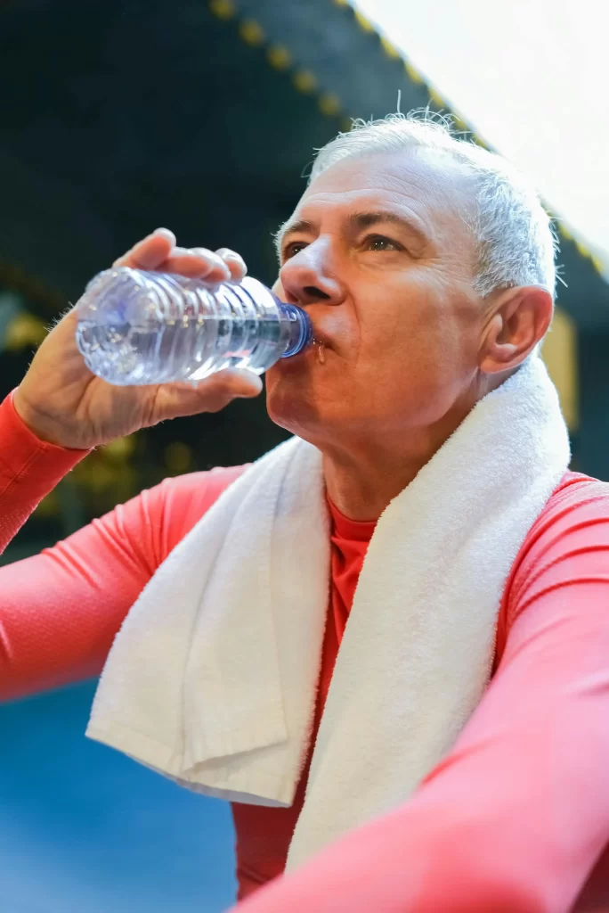 Older man drinking water after exercising, highlighting hydration and recovery while training for your second act.