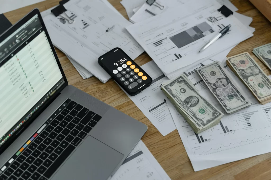 Laptop, cash, calculator, and financial papers showing the money-management side of the modern creative starter stack.