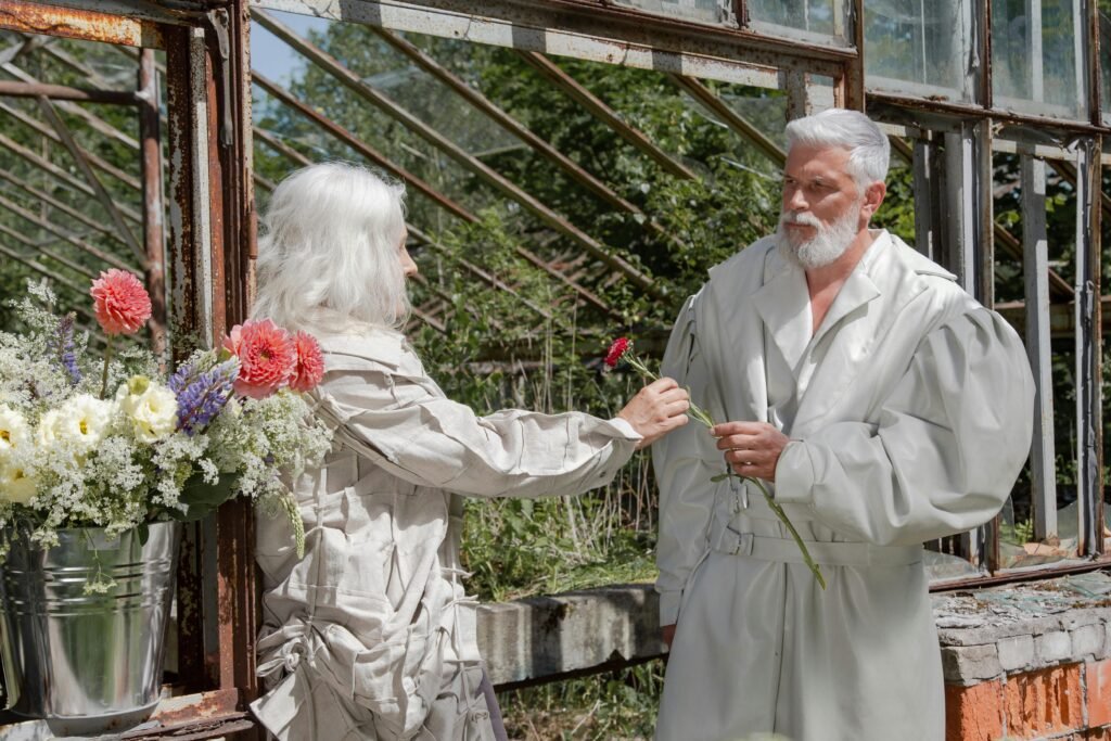 Older woman handing a flower to an older man inside a rustic greenhouse