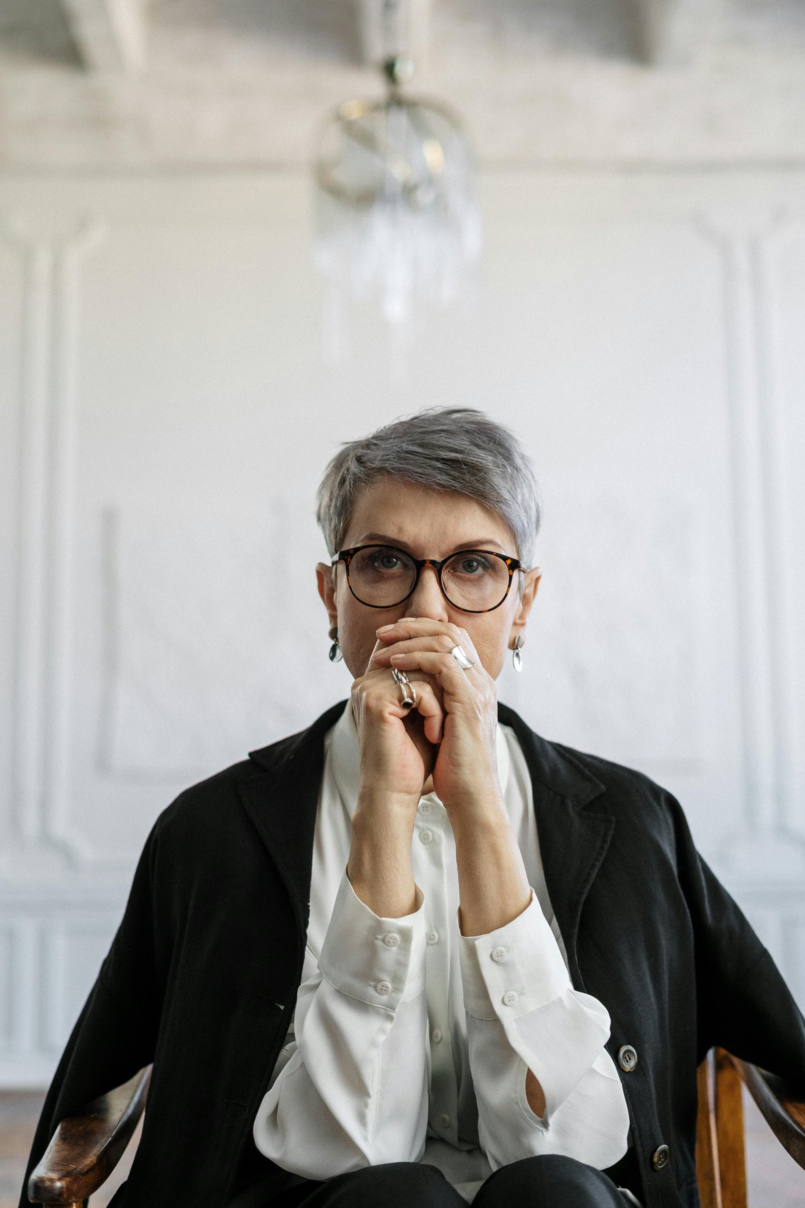 Confident woman in midlife sitting with her hands together, looking ahead with focus and clarity.