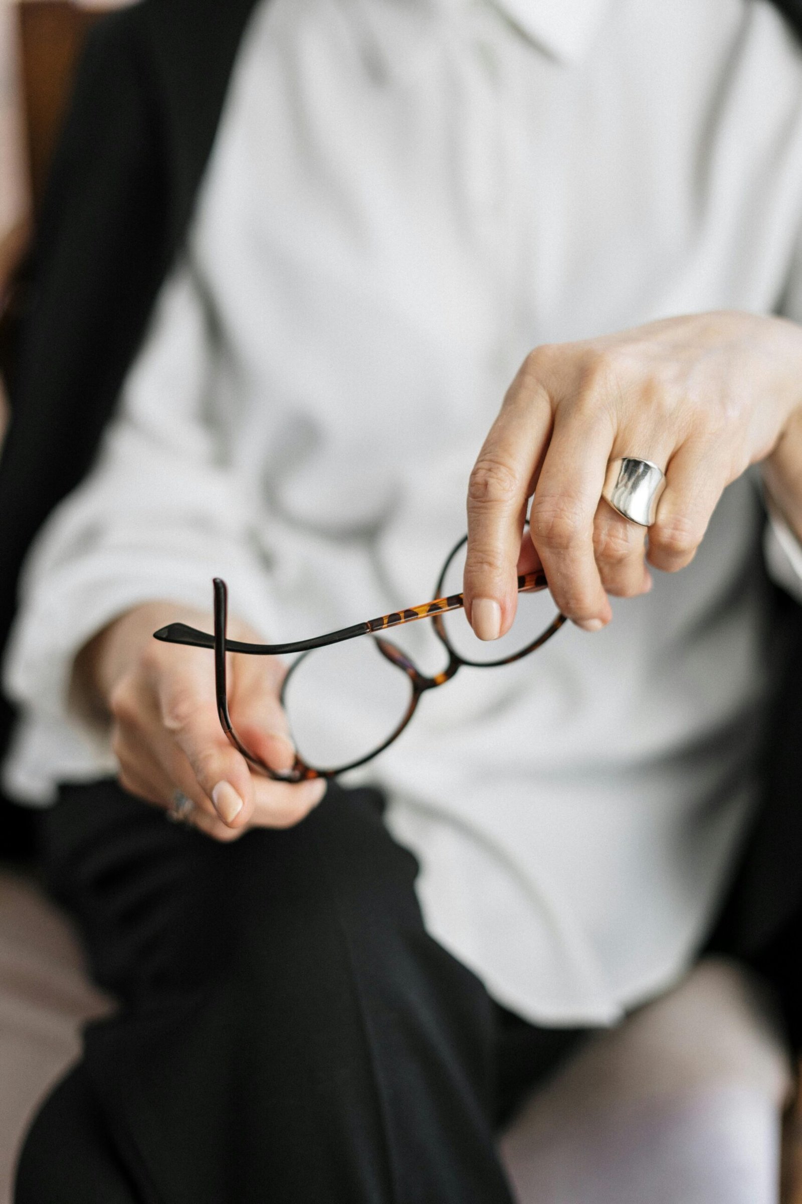 Close-up of a mature woman’s hands holding eyeglasses, symbolizing reflection and pause in midlife.