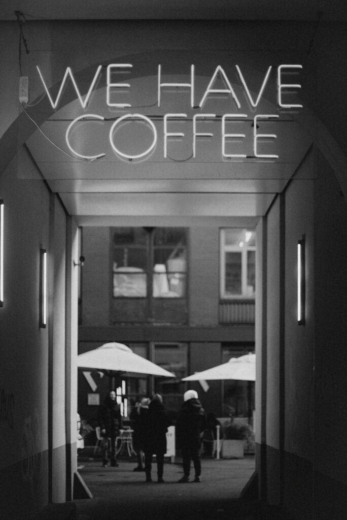 Neon sign reading “We Have Coffee” in a quiet passageway, symbolizing comfort rituals while traveling