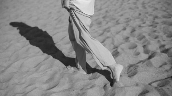 Person walking barefoot on sand, reflecting on movement, pause, and travel
