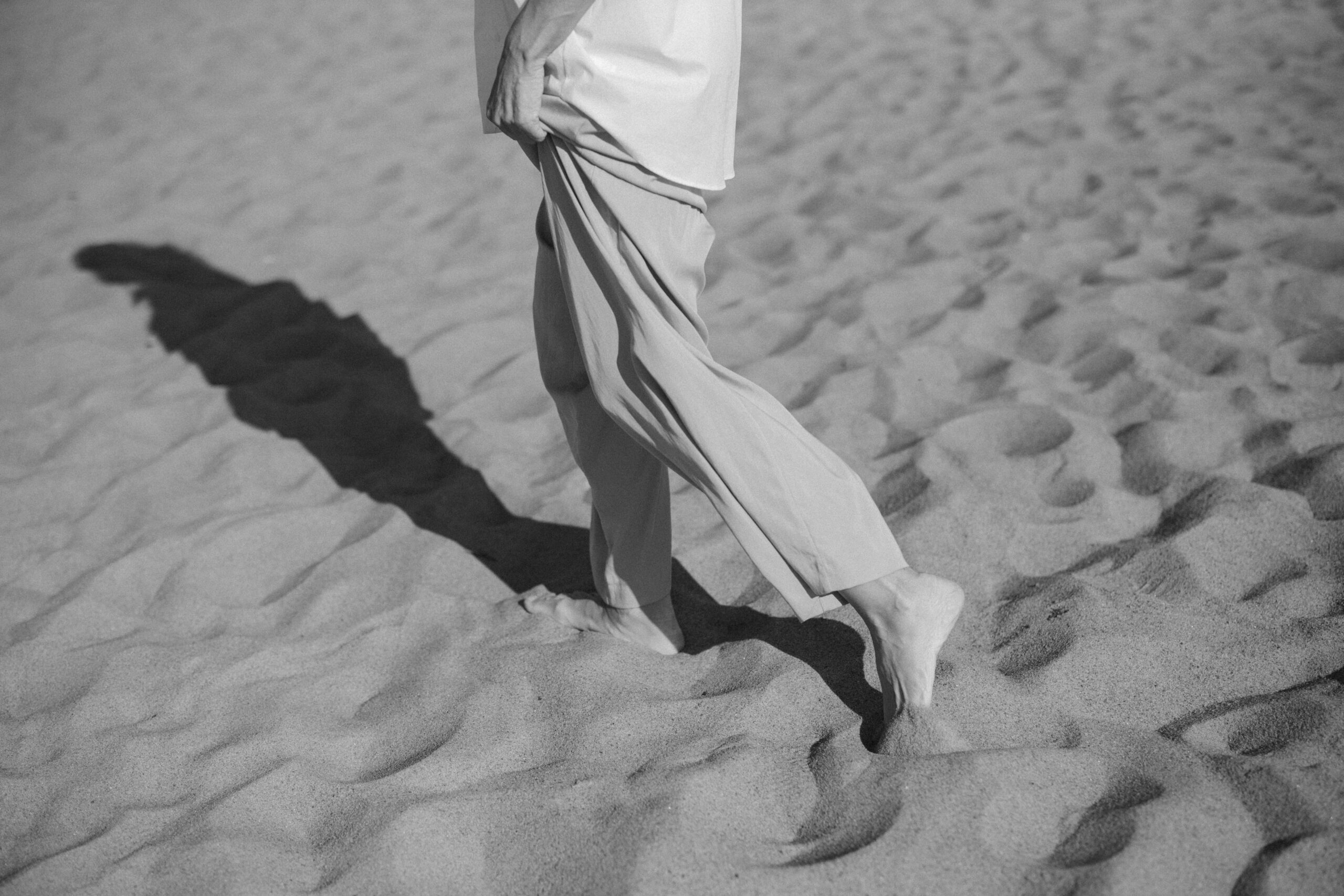 Person walking barefoot on sand, reflecting on movement, pause, and travel
