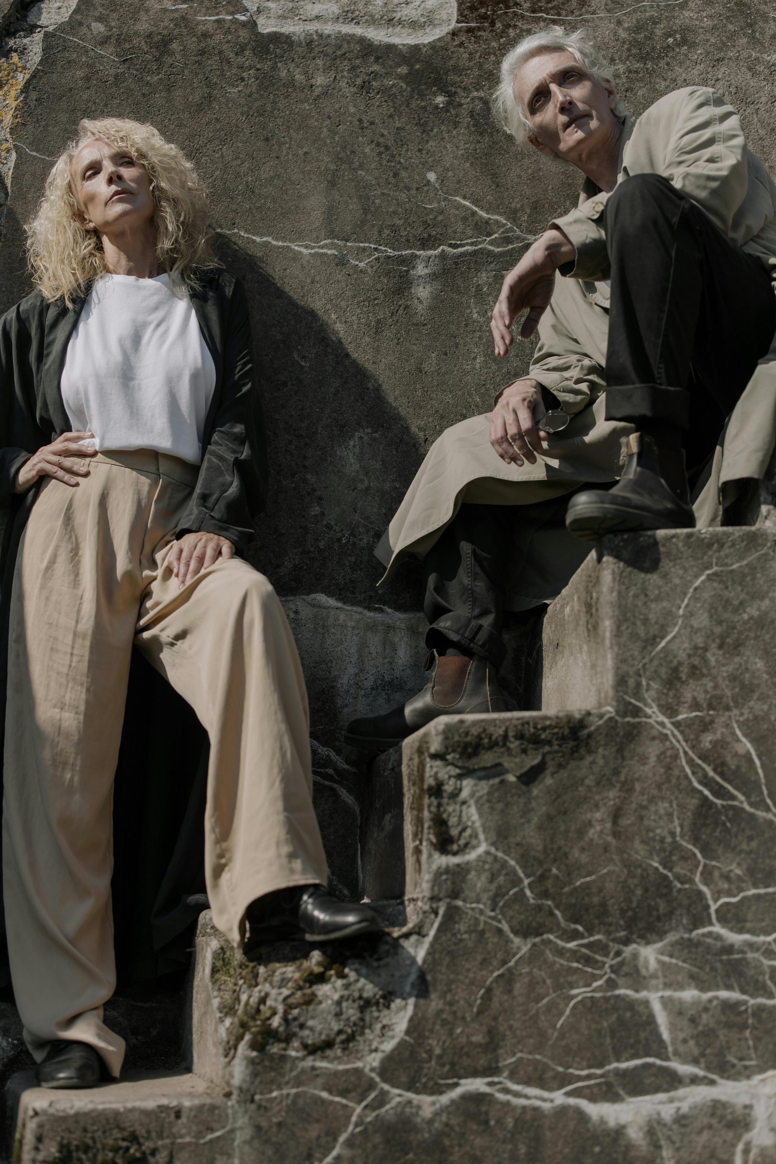 Mature couple sitting apart on stone steps, appearing reflective and emotionally distant in midlife