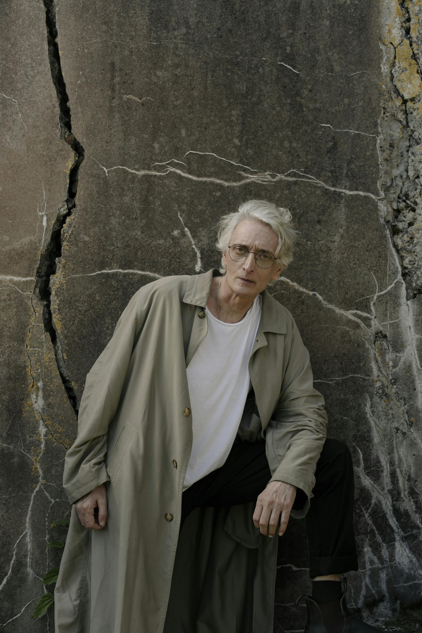 Middle-aged man standing against a cracked stone wall, looking thoughtful during a period of personal reflection
