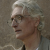 Close-up portrait of an older man with gray hair and glasses, looking off into the distance thoughtfully