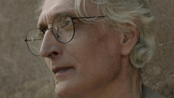 Close-up portrait of an older man with gray hair and glasses, looking off into the distance thoughtfully