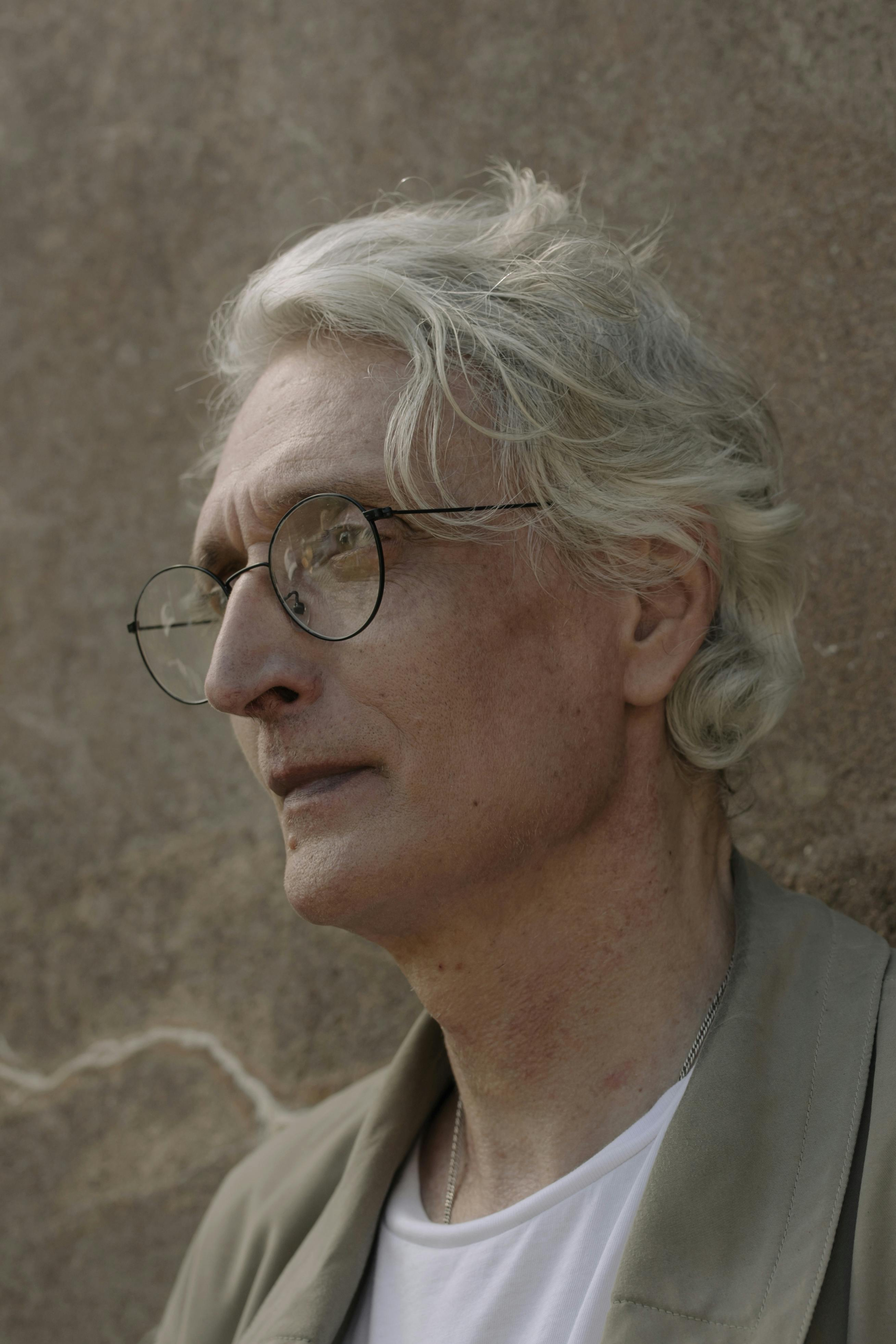 Close-up portrait of an older man with gray hair and glasses, looking off into the distance thoughtfully