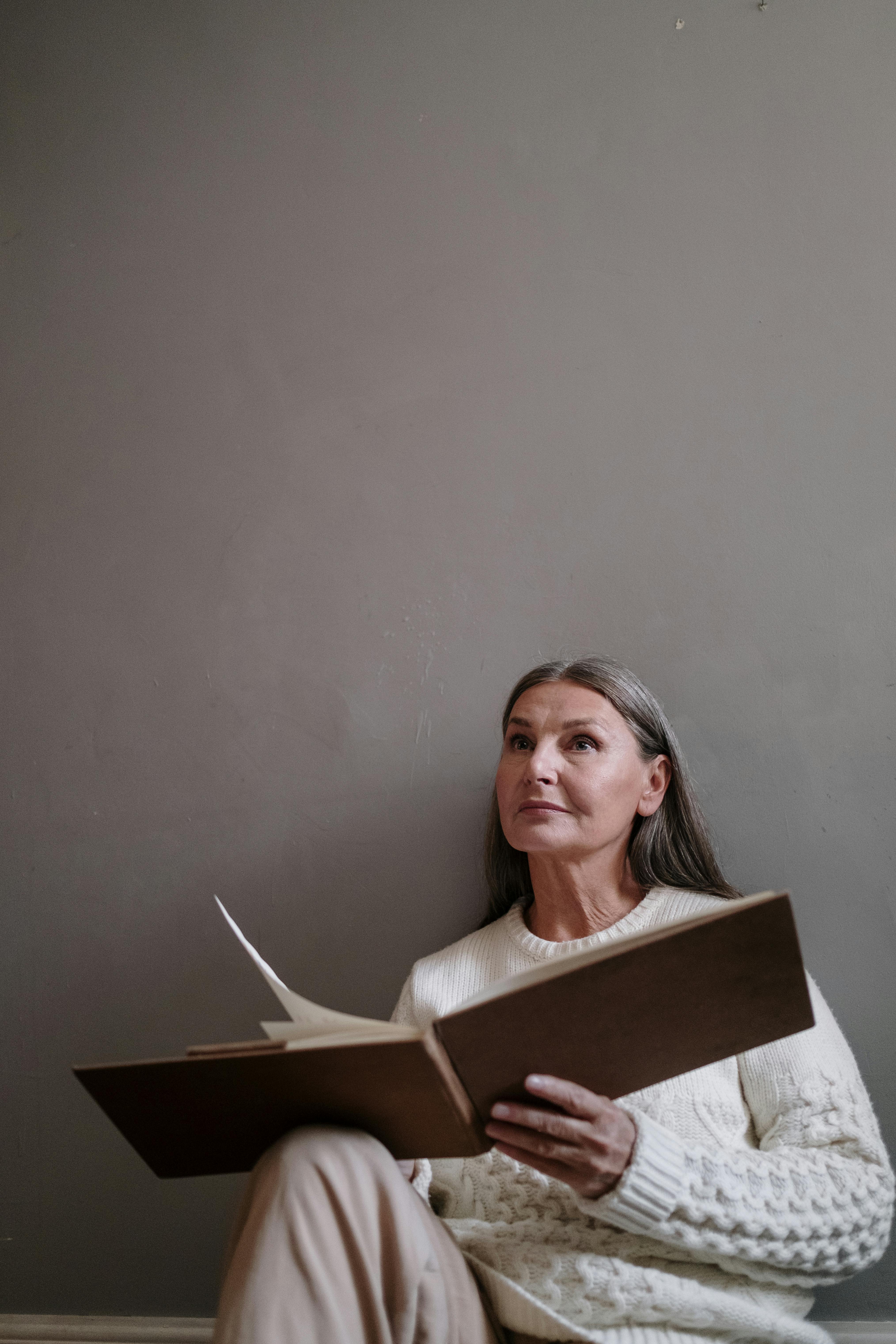 Older woman sitting on the floor reading a large book and reflecting calmly.