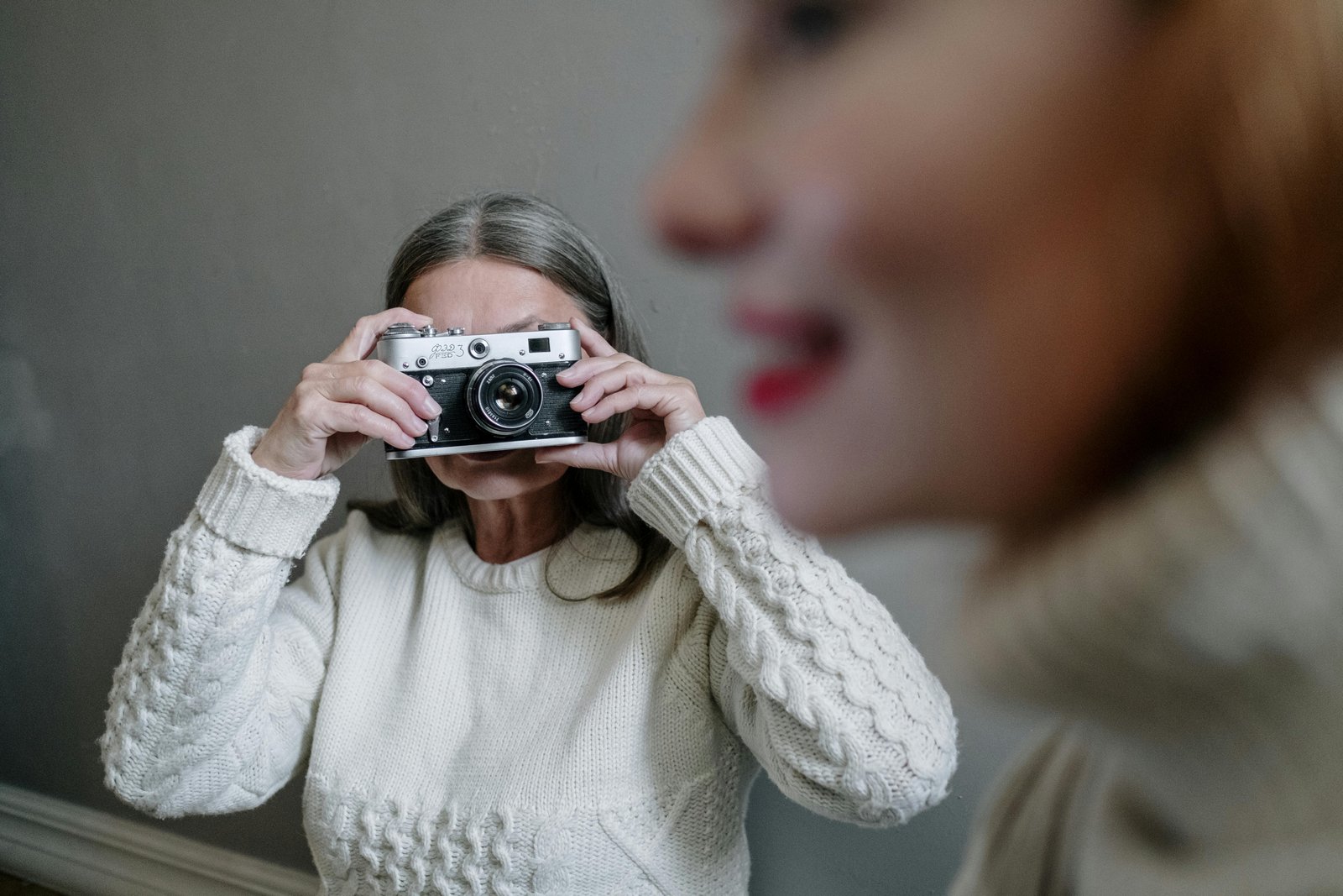 Older woman holding a vintage film camera and taking a photograph indoors.