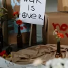 Peaceful protest setup with a handwritten ‘War Is Over’ sign surrounded by flowers and cardboard boxes.
