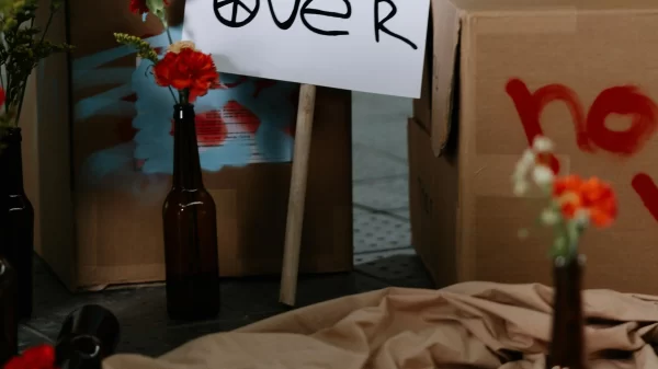 Peaceful protest setup with a handwritten ‘War Is Over’ sign surrounded by flowers and cardboard boxes.