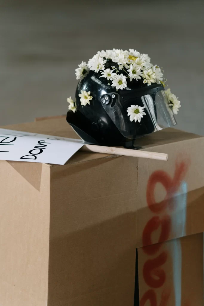 Black riot helmet decorated with white daisies placed on a cardboard box during a peace demonstration.