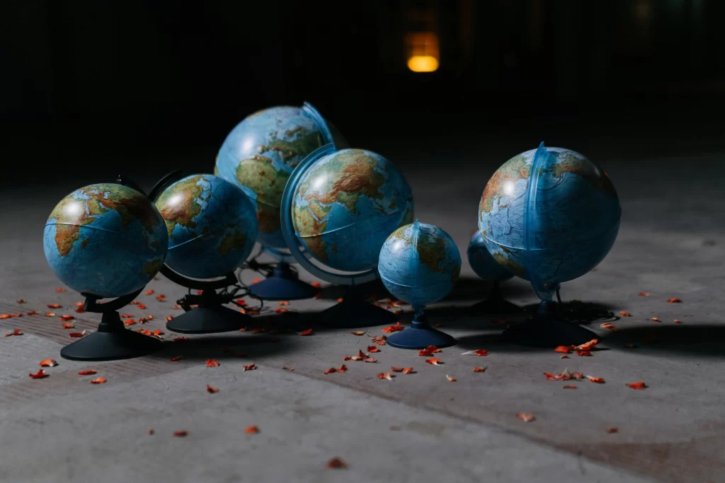 Group of world globes arranged on a dimly lit floor with scattered red petals.