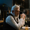 Older man sitting alone at a table in a dimly lit restaurant, looking thoughtful and reflective