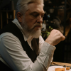 Older man sitting at a table, looking thoughtful and pensive in a dimly lit room