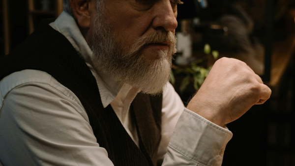 Older man sitting at a table, looking thoughtful and pensive in a dimly lit room