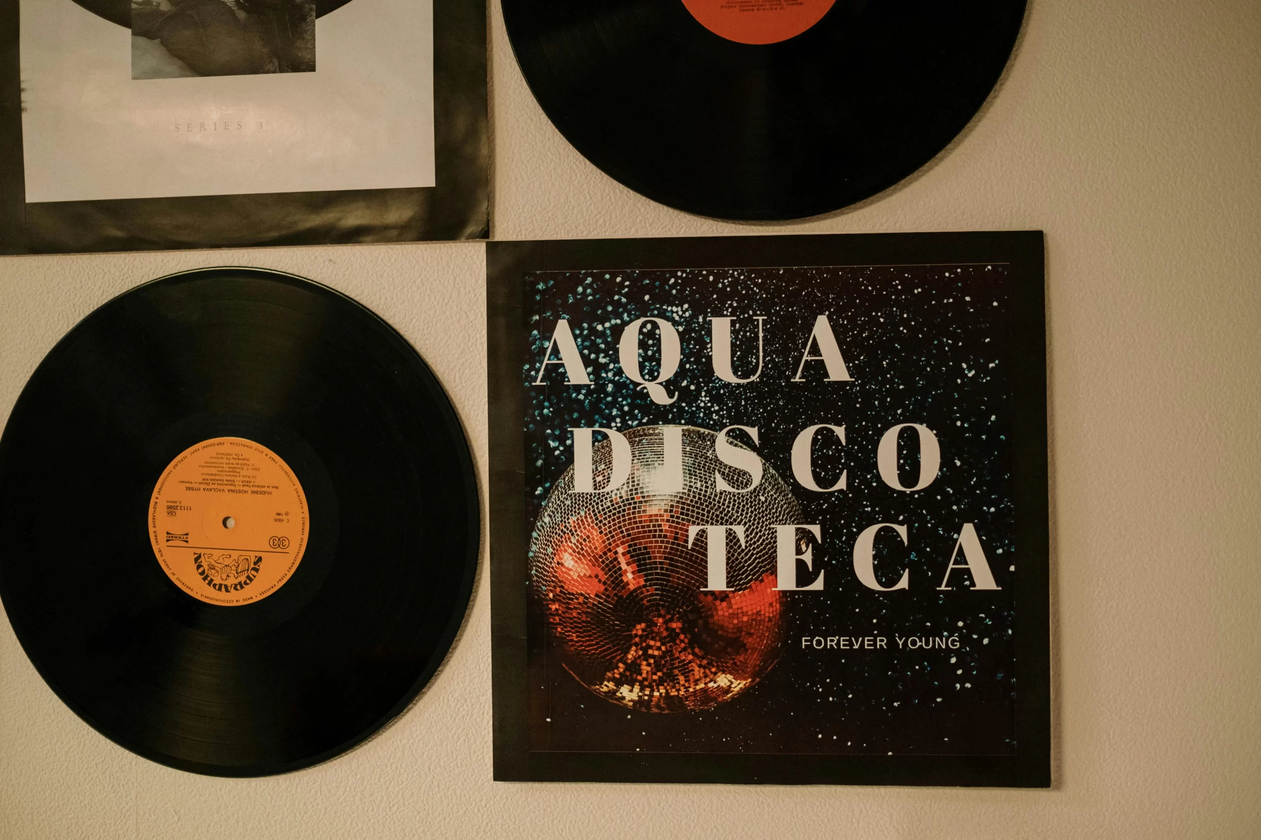 A wall decorated with vinyl records and an album cover titled “Aqua Discoteca Forever Young.”
