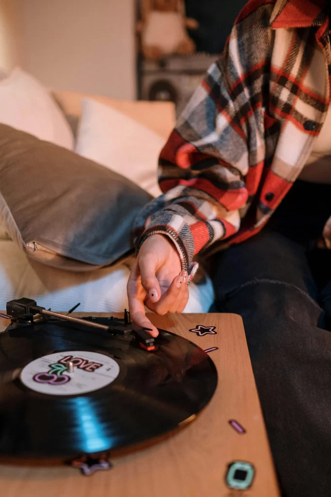 A person in a plaid shirt adjusting the needle on a vinyl record player at home.