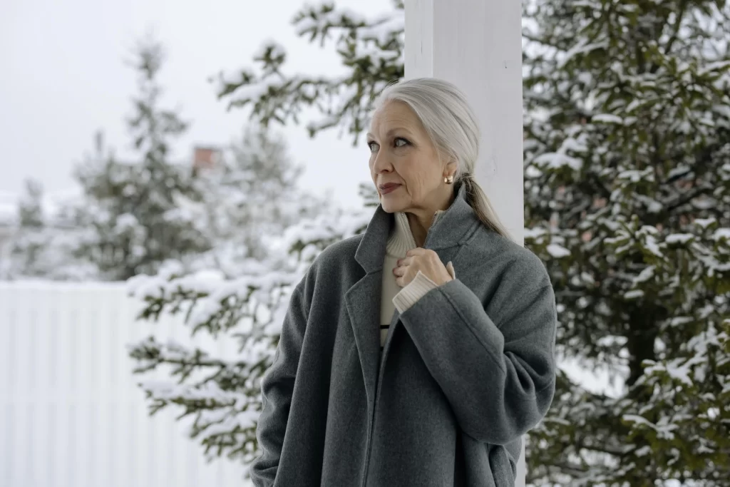 Elegant older woman standing outside in winter wearing a structured gray coat, showcasing timeless outerwear.