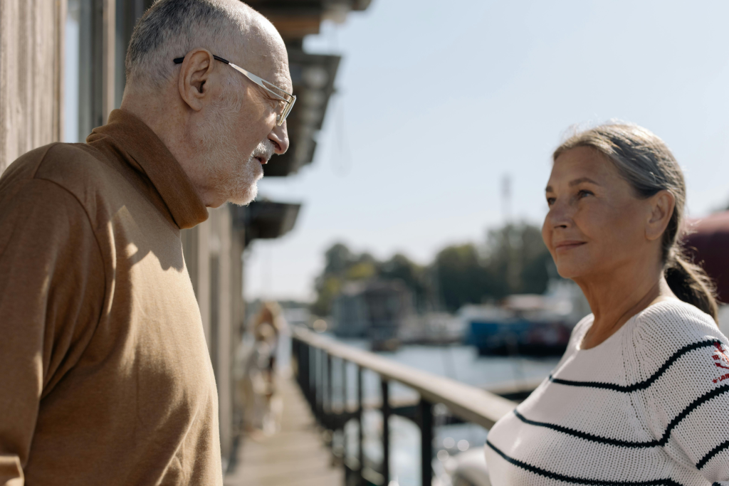 Older man and woman talking face to face outdoors by the water, reflecting on life and change