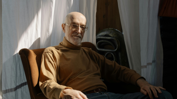 Older man sitting in a chair near a window, looking thoughtful during a quiet moment at home