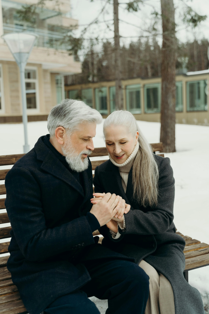 Senior couple sitting on a bench holding hands in winter