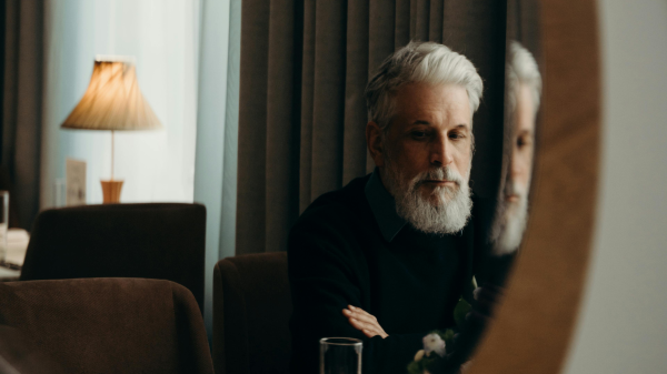 Man in his 50s looking at his reflection, reflecting on body composition changes and muscle loss