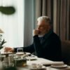 Man in his 60s sitting at a dining table, reflecting quietly in a calm, minimalist home