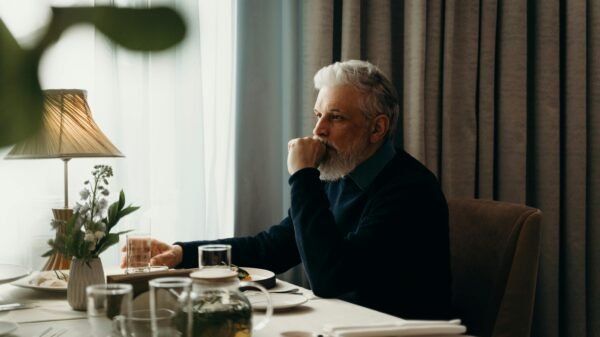 Man in his 60s sitting at a dining table, reflecting quietly in a calm, minimalist home