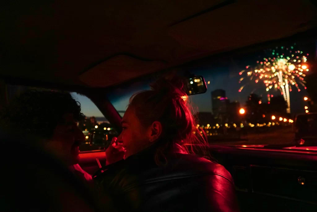 Couple sitting in the backseat of a car watching fireworks through the window at night.