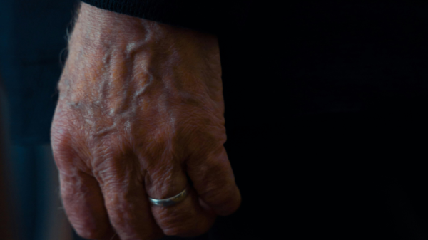 Close-up of an elderly man’s hand with visible veins and a silver wedding ring.