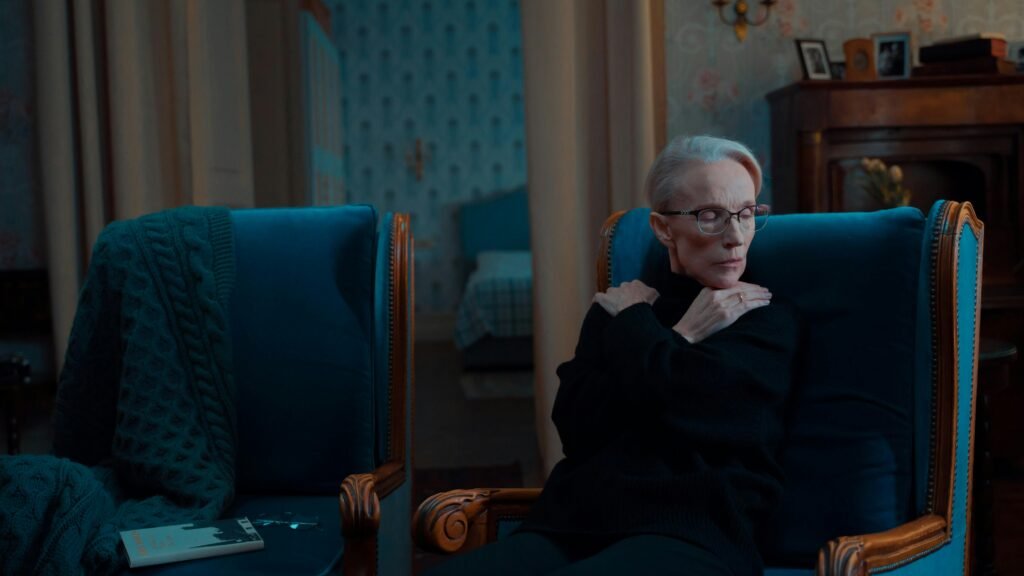 Older woman sitting alone in an armchair, reflecting on future plans in a quiet, dimly lit room