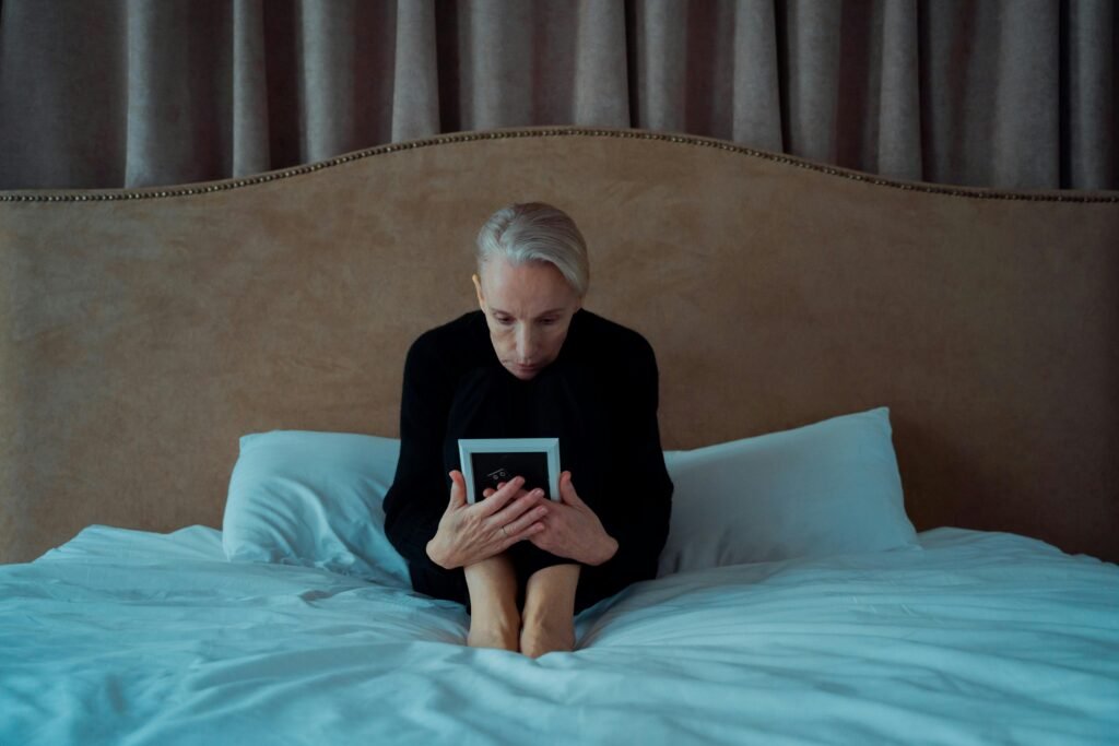 Older woman sitting on a bed holding a photo frame, contemplating life changes and planning ahead
