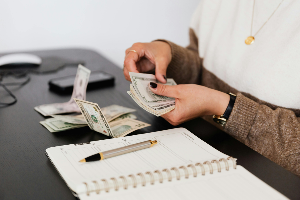 Person counting cash beside a notebook, showing budgeting and financial planning