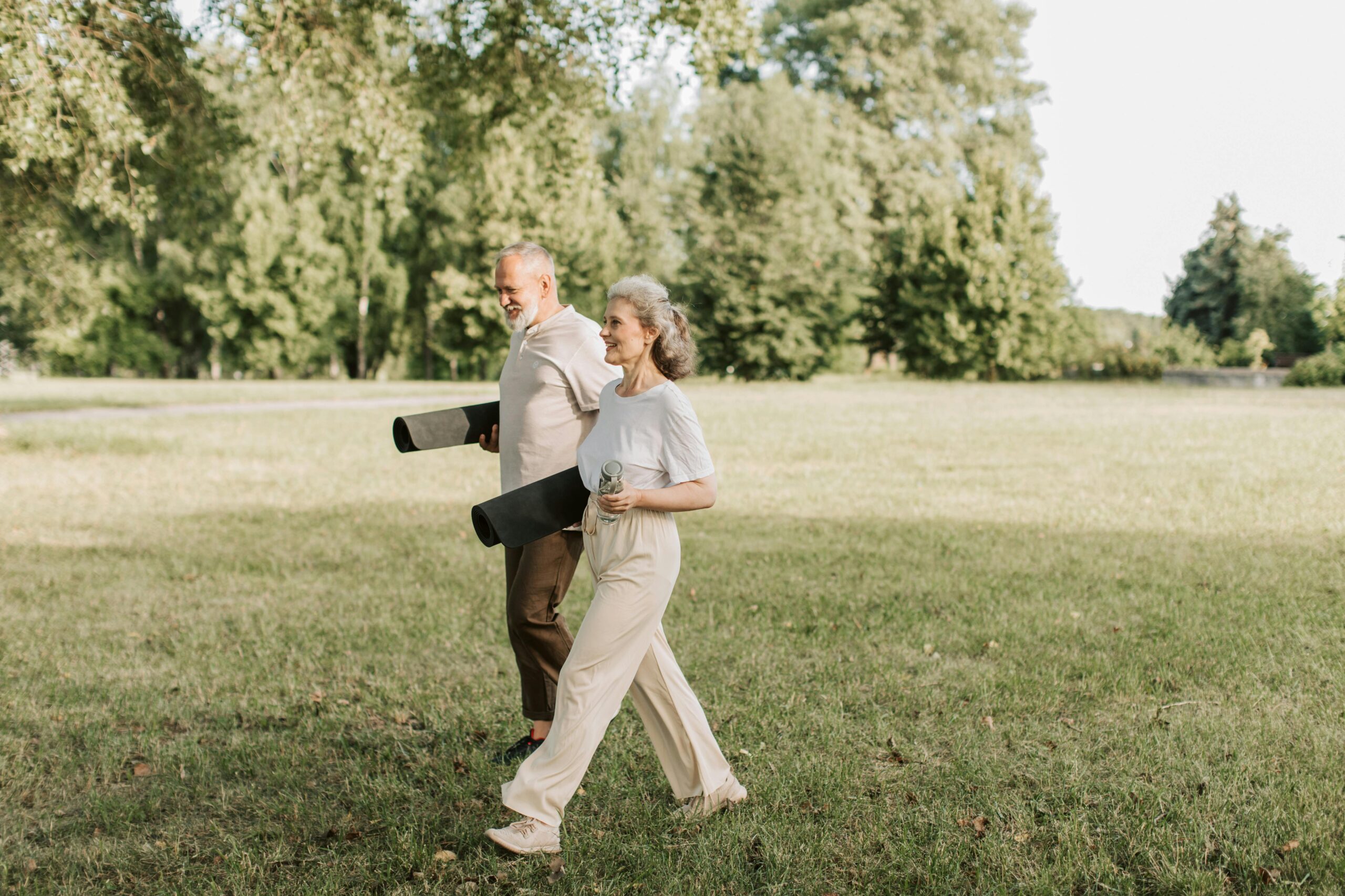 Mature couple walking outdoors carrying yoga mats during a relaxed fitness routine